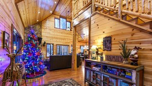 Interior acogedor de una cabaña de troncos con un árbol de Navidad decorado, un letrero de bienvenida familiar y una rústica escalera de madera.