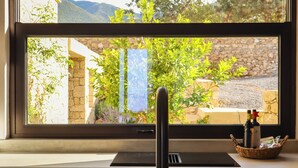 A kitchen with a window overlooking a garden and mountains. - Olive Villas (West Mani)