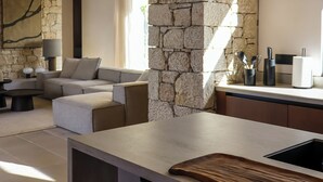 A modern living room with a stone accent wall, a sofa, and a dining area with a bar. - Olive Villas (West Mani)