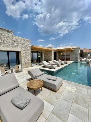 A poolside area with lounge chairs and a stone building. - Olive Villas (West Mani)