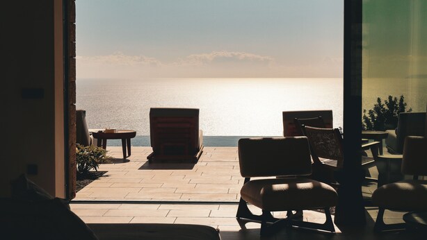 An open patio with a view of the sea, furnished with chairs and a table. - Olive Villas (West Mani)
