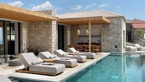 A modern poolside area with stone walls, lounge chairs, and a dining area. - Olive Villas (West Mani)