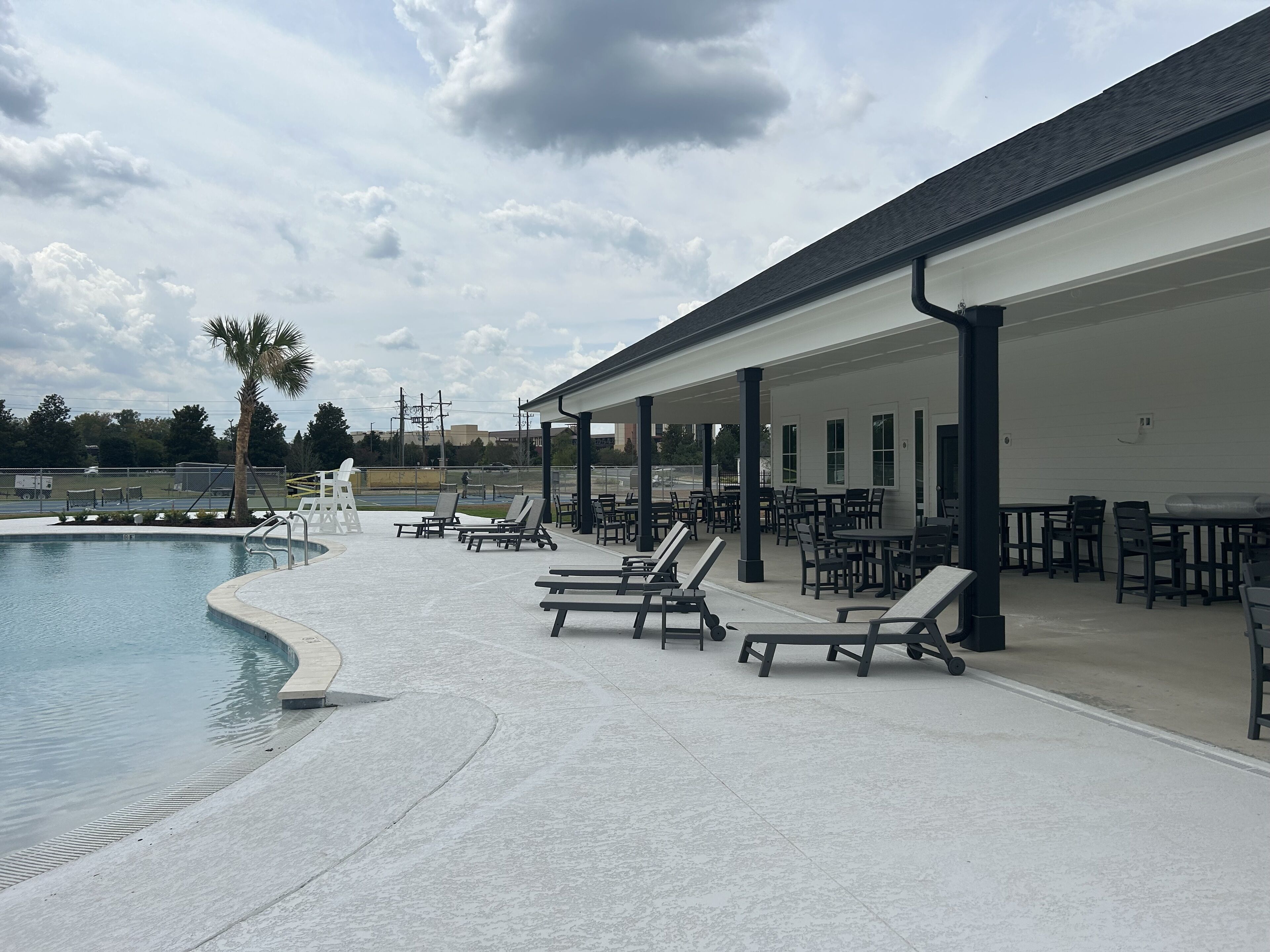 A poolside area with lounge chairs and tables, a covered seating area, and a view of the pool.
