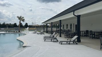 A poolside area with lounge chairs and tables, a covered seating area, and a view of the pool.