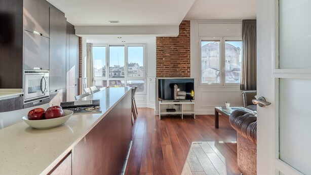 A modern kitchen with a central island, a dining area with a sofa, and a TV. - Enjoybcn Fira Apartment (Barcelona)