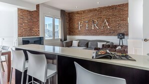 A modern kitchen with a brick wall, a large island with bar stools, and a sofa in the living area. - Enjoybcn Fira Apartment (Barcelona)