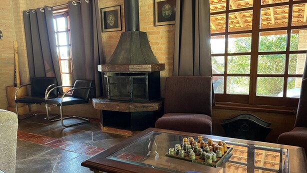 Une pièce chaleureuse avec une cheminée, des fauteuils confortables et un jeu d’échecs posé sur une table en verre.
