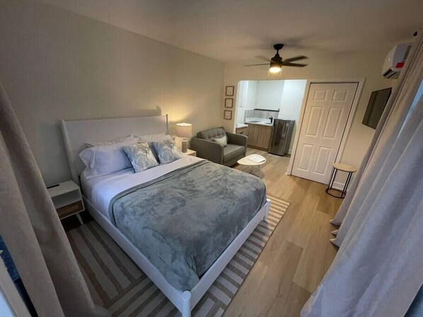 Un dormitorio moderno con una cama grande, un pequeño sofá, un escritorio y un ventilador de techo.