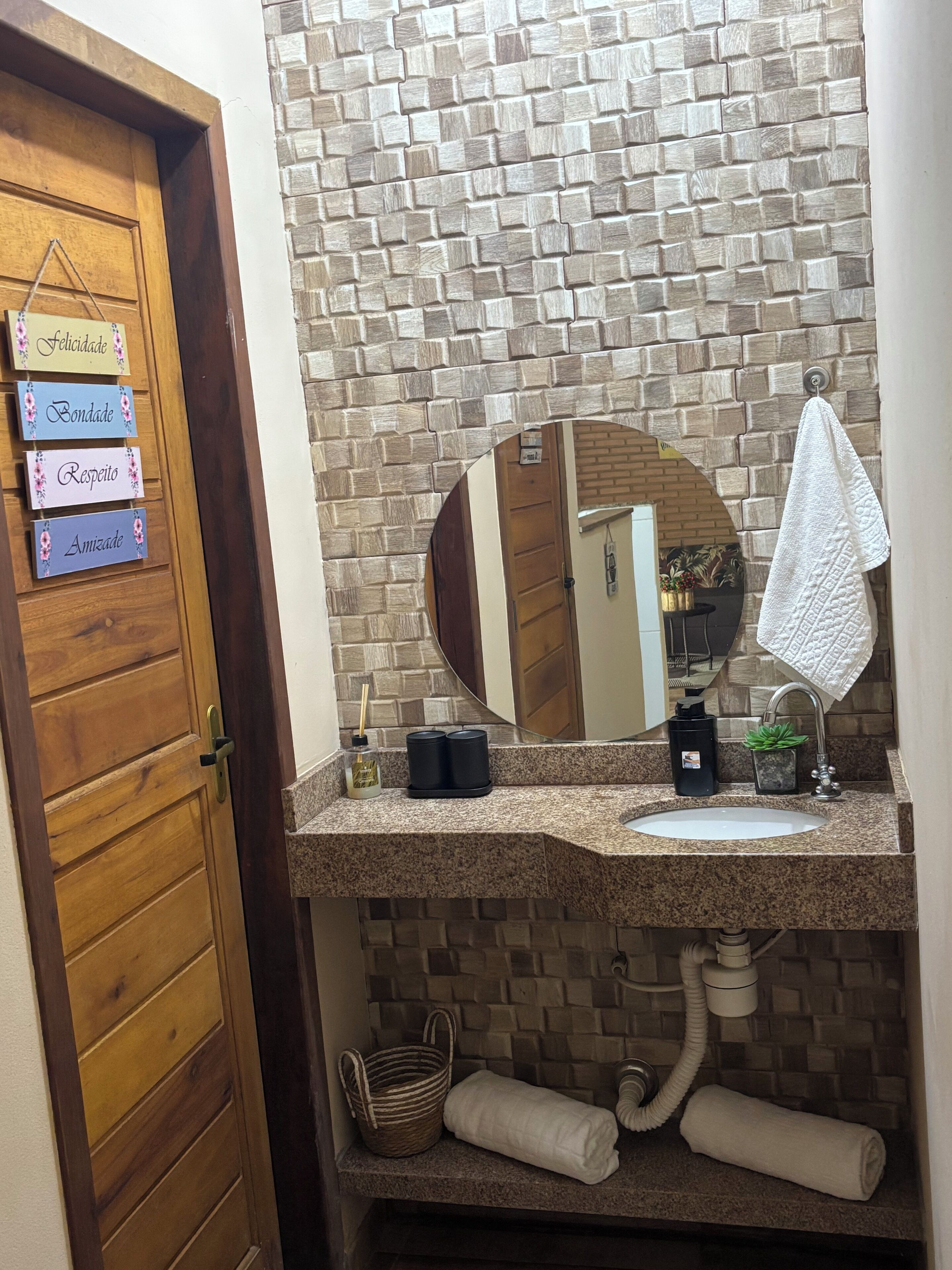 Um banheiro com porta de madeira, espelho, pia e toalha pendurada na parede.