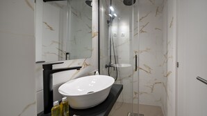 Et moderne badeværelse med en stor, hvid vask, bordplade i sort og et bruseområde med glasvægge.