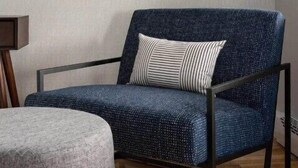 Un sillón azul con un cojín a rayas, un otoman redondo pequeño y un cuadro en la pared.