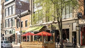 Una calle con una zona de estar al aire libre de madera, un coche y edificios con diversos comercios.