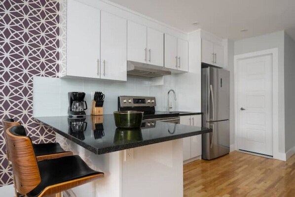 Una cocina moderna con armarios blancos, un refrigerador de acero inoxidable, una encimera negra y un salpicadero con estampado.