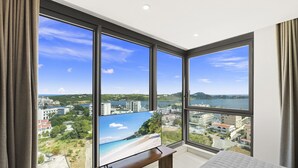Une chambre dotée de grandes fenêtres donnant sur une plage et offrant une vue sur la ville.