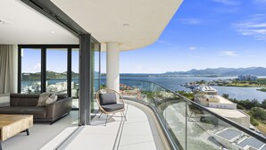 A modern balcony with a glass railing, a sofa, and a chair, overlooking a body of water and distant mountains. - B-1603 Stunning two bedroom apartment with panoramic views (Cupecoy)