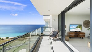 Un balcon avec vue sur l’océan, une chaise en osier, un téléviseur et un meuble en bois.