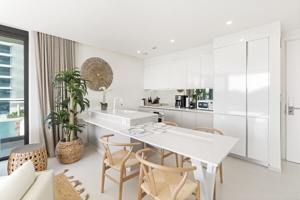 Une cuisine moderne avec des meubles blancs, un plan de travail blanc et un coin repas doté de chaises en bois.