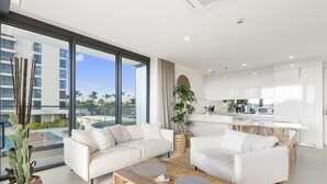 A modern living room with white sofas, a wooden coffee table, and a large window offering a view of a cityscape. - B-102 Stunning ocean view unit (Cupecoy)
