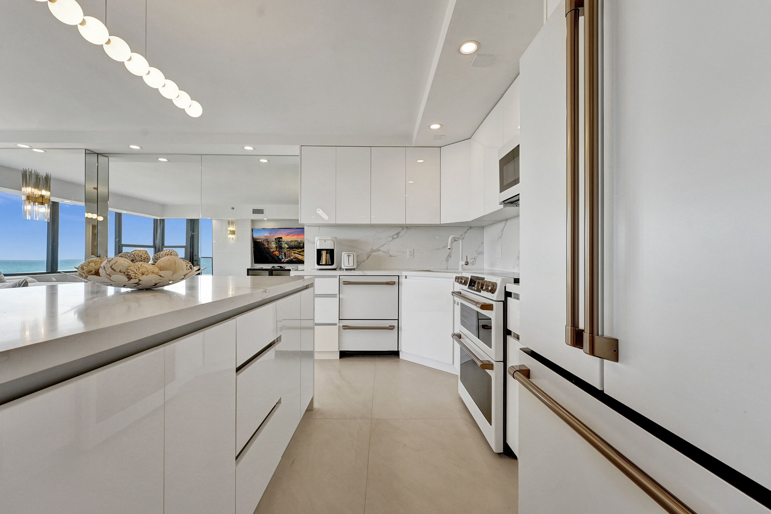 Une cuisine moderne avec des meubles blancs, un grand îlot central et une vue sur l’océan.