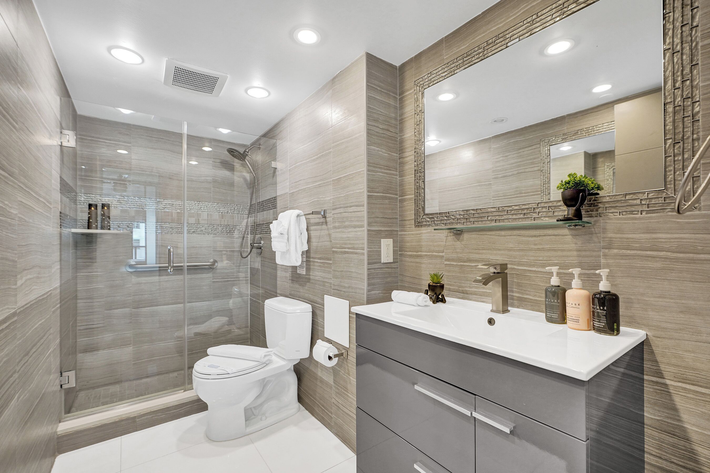 Une salle de bain moderne avec une douche à parois de verre, des toilettes blanches, un meuble-lavabo avec un miroir et des articles de toilette.