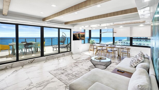 A spacious living area with a large balcony overlooking the sea, featuring a sofa, dining table, and chairs. - Alexander Hotel (Miami Beach)