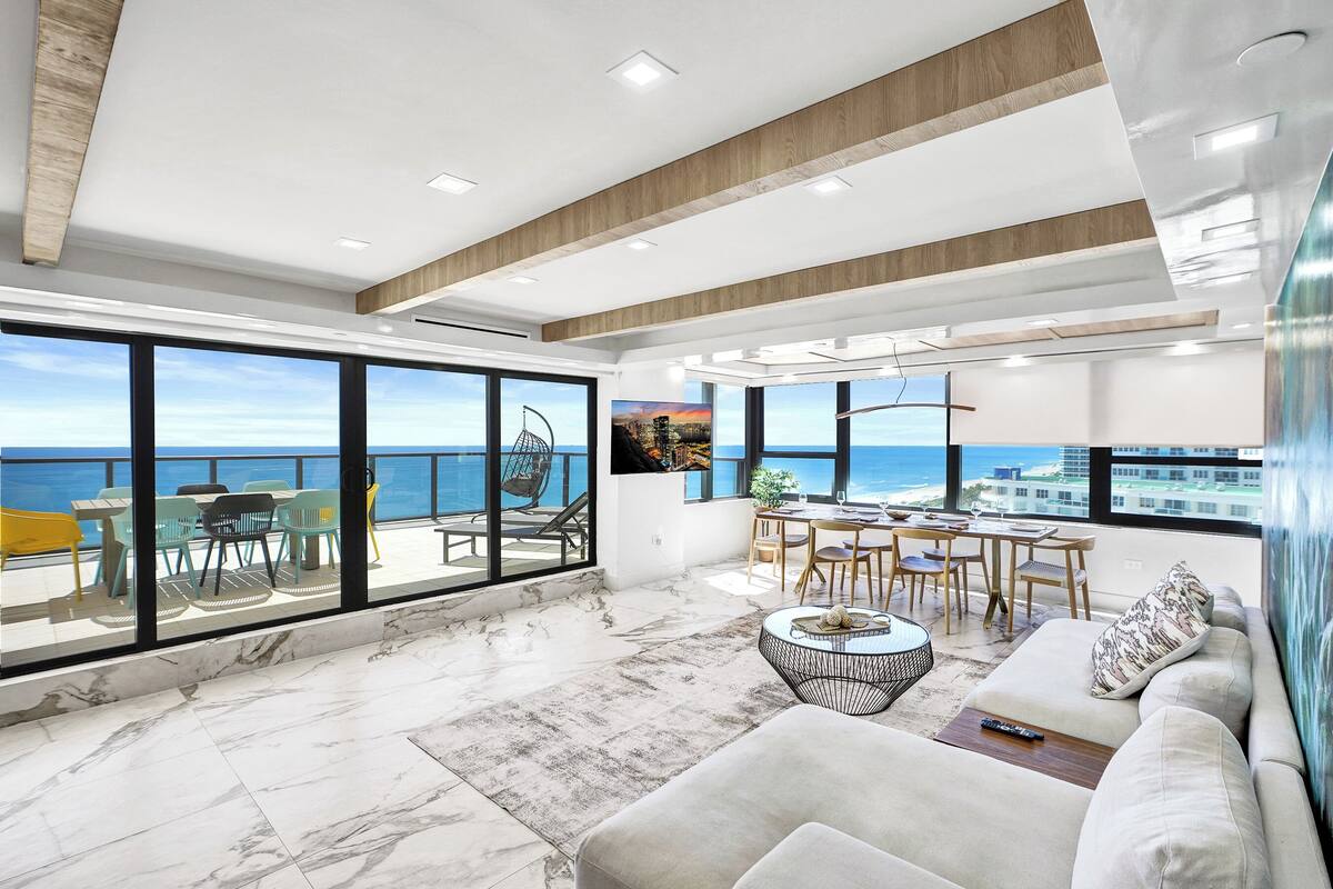 Uma sala de estar espaçosa com uma varanda grande e vista para o mar, com sofá, mesa de jantar e cadeiras.