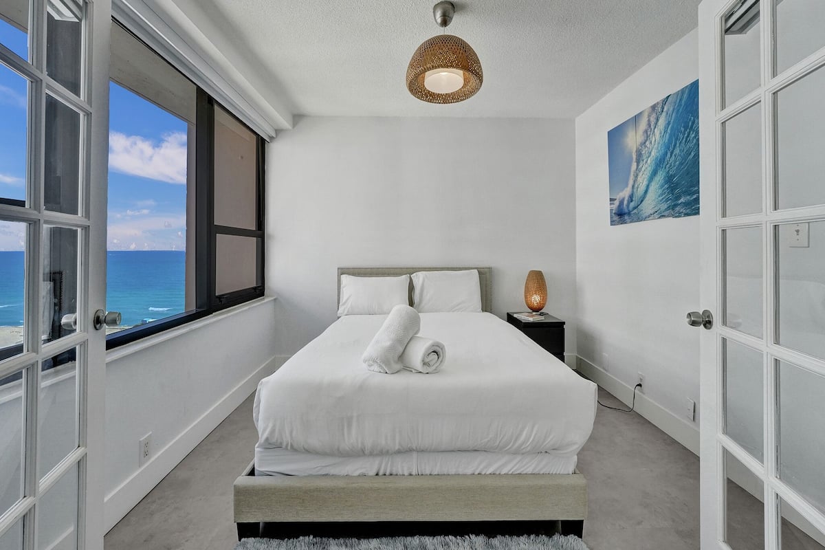 Quarto com cama, mesa de cabeceira, abajur e uma pintura.