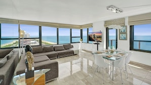 A modern living room with a large window, a sofa, a glass dining table, and a TV. - Alexander Hotel (Miami Beach)