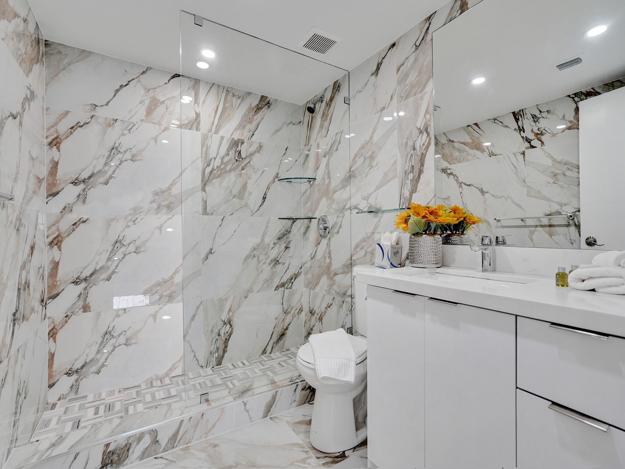 A modern bathroom with marble walls, a glass shower enclosure, and a white vanity with a mirror.
