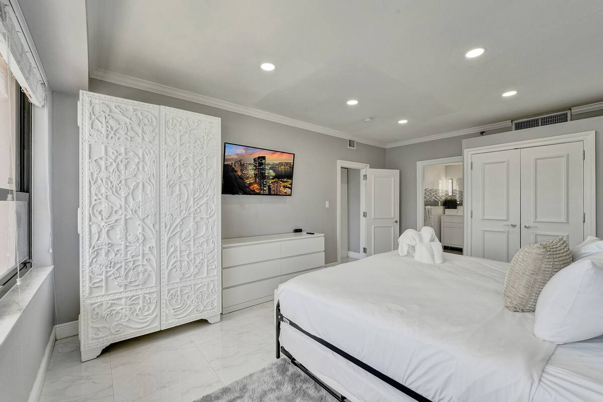 Um quarto com uma cama grande, um guarda-roupa com detalhes entalhados, uma cômoda e uma pintura com vista para a cidade na parede.