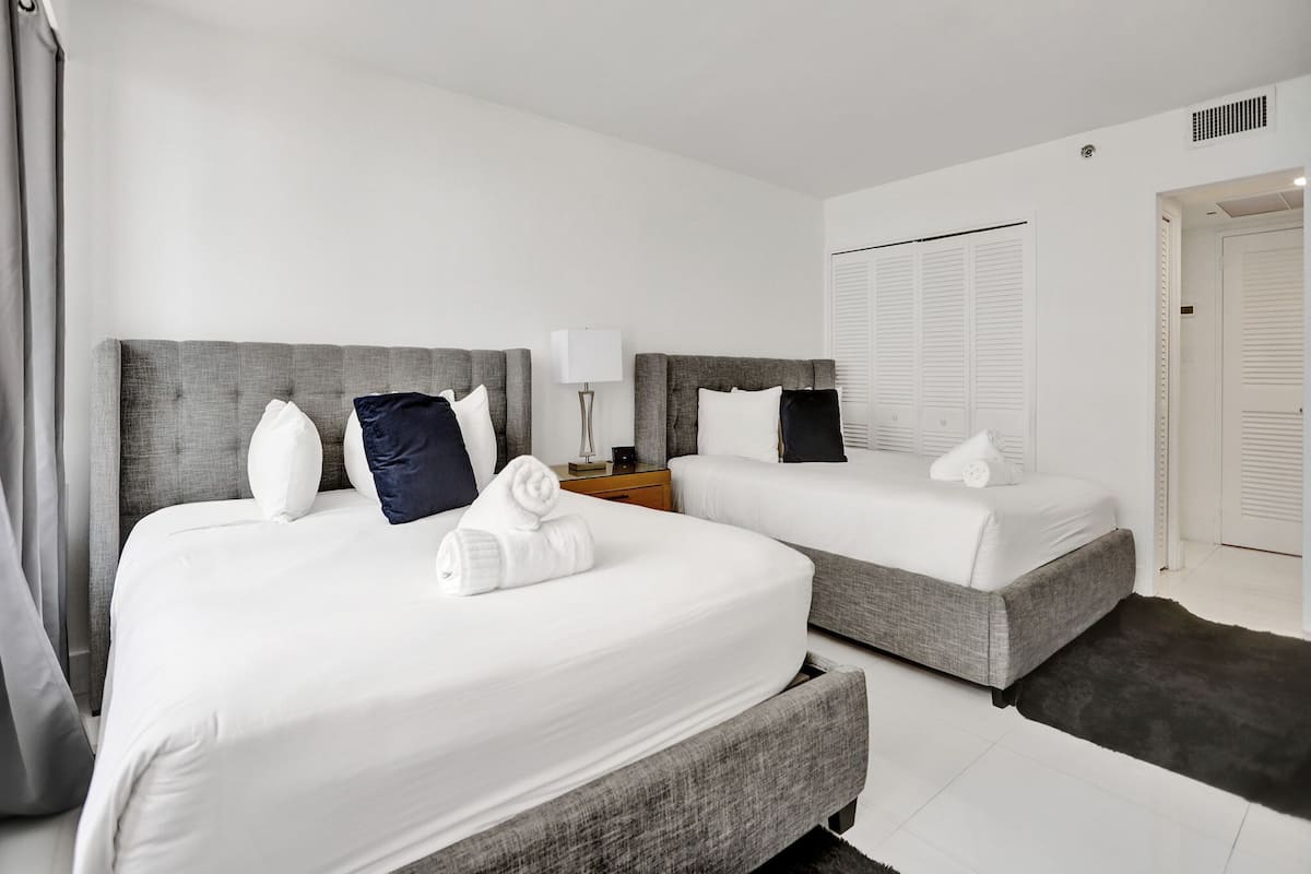 Quarto de hotel com duas camas, uma mesa de cabeceira, um abajur e um guarda-roupa.