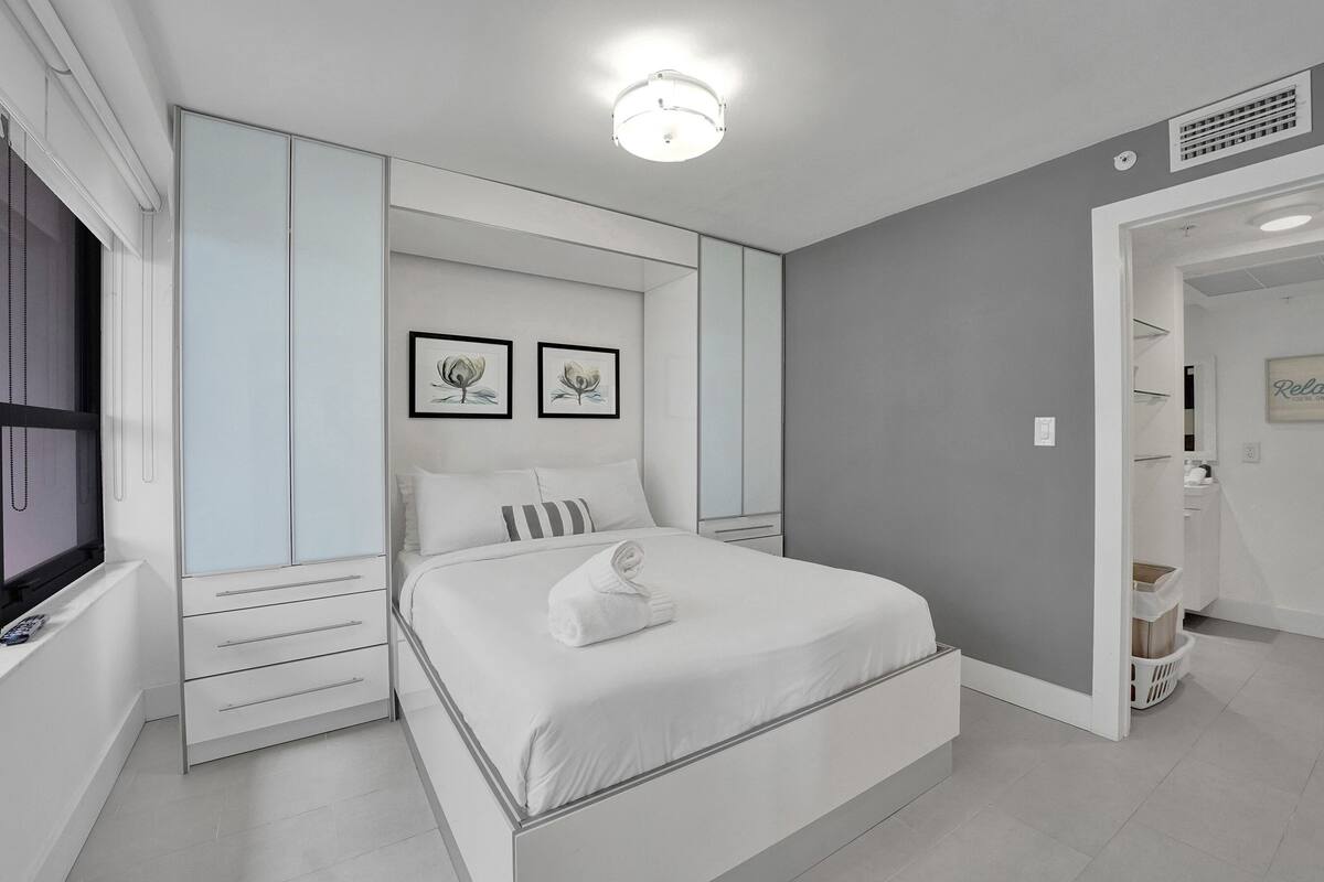 Quarto moderno com cama, mesas de cabeceira, guarda-roupa e uma luminária no teto.