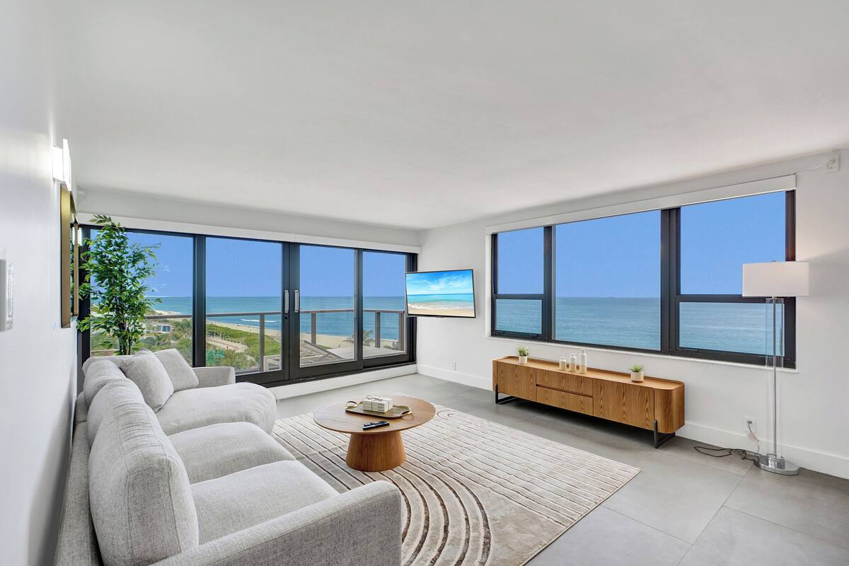 Uma sala de estar moderna com uma janela ampla que oferece vista para a praia e o oceano.