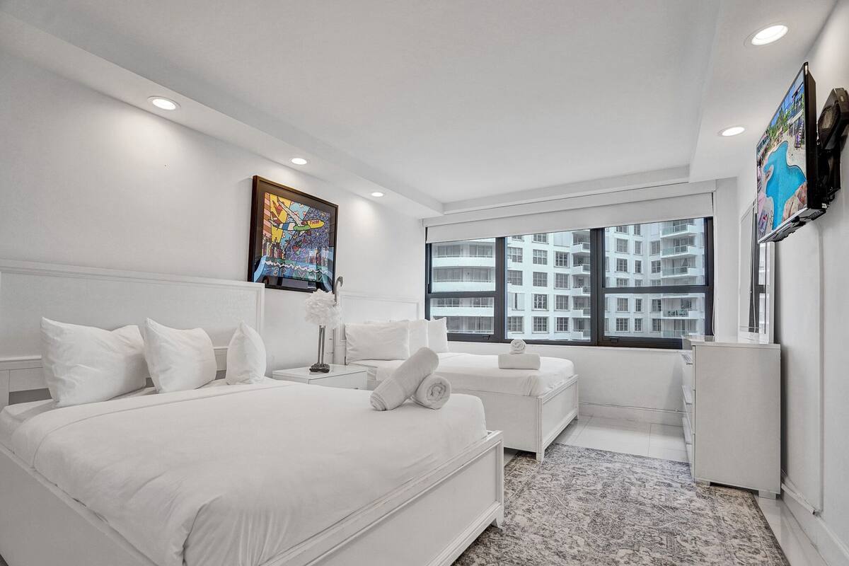 Quarto de hotel moderno com uma cama grande, uma escrivaninha pequena, uma TV e uma janela com vista para a cidade.