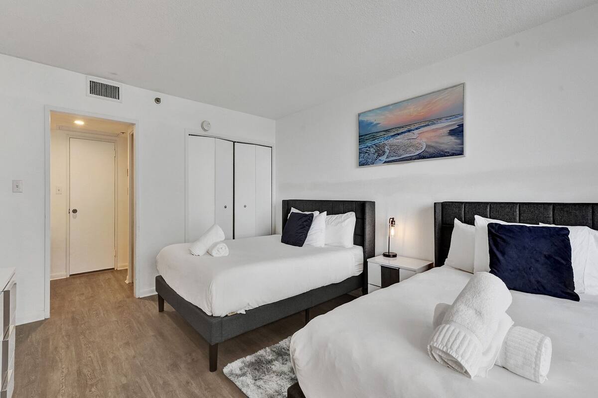 Quarto de hotel com duas camas, um quadro, uma porta e um interruptor de luz.