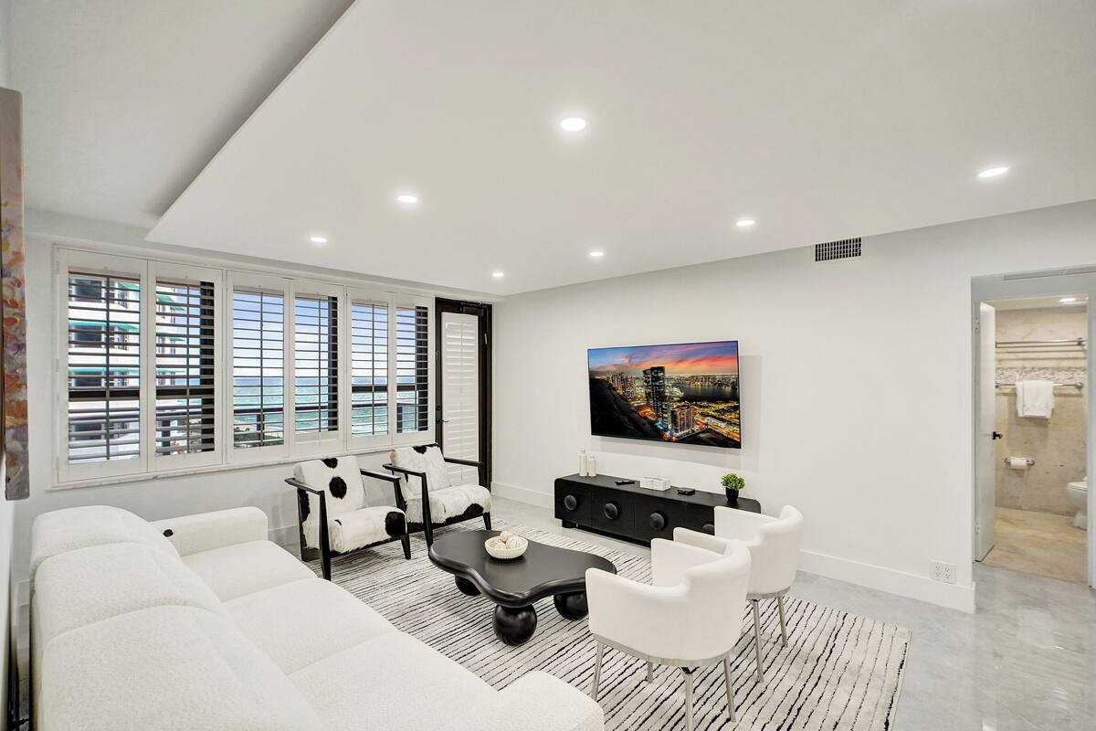 Uma sala de estar moderna com um sofá, uma mesa de centro e uma TV fixada na parede.
