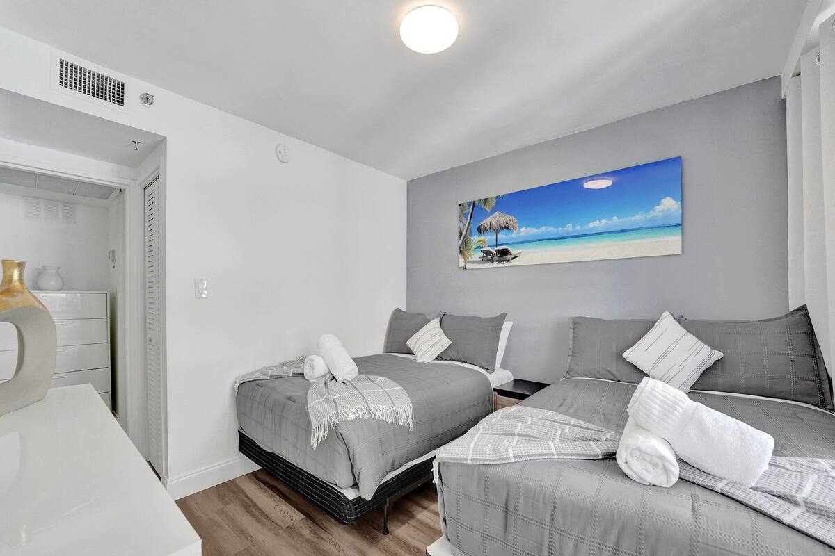 Quarto com duas camas, um quadro de uma praia e um aparador branco.