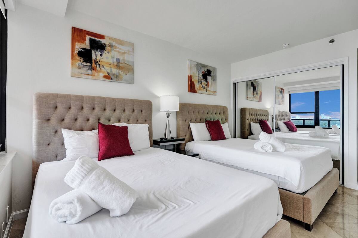 Quarto de hotel com duas camas, um espelho grande e obras de arte nas paredes.