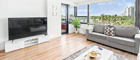 Una sala de estar moderna con un televisor de pantalla plana, un sofá gris y un ventanal con vistas a la ciudad.