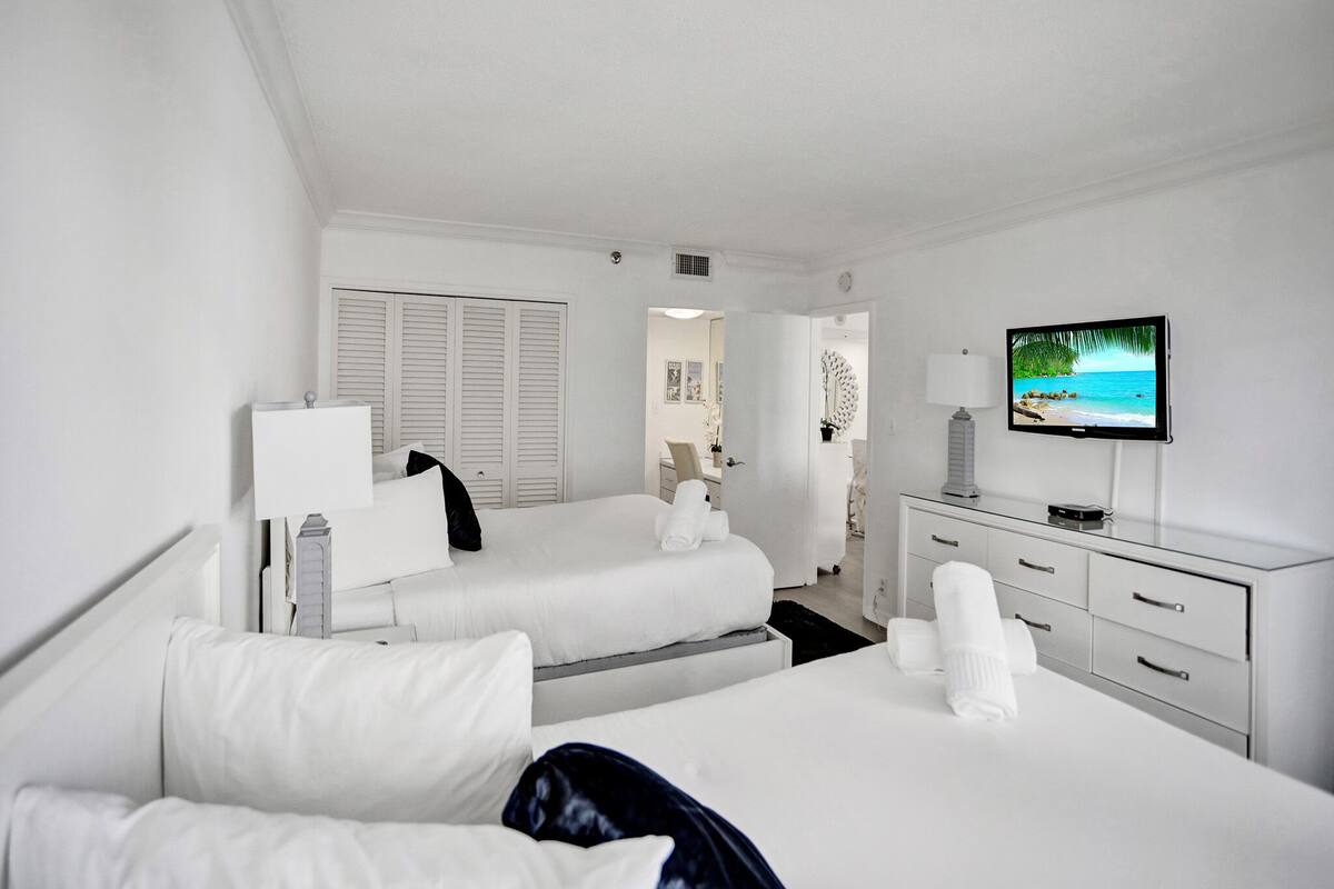 Quarto de hotel com duas camas, televisão, escrivaninha e guarda-roupa.