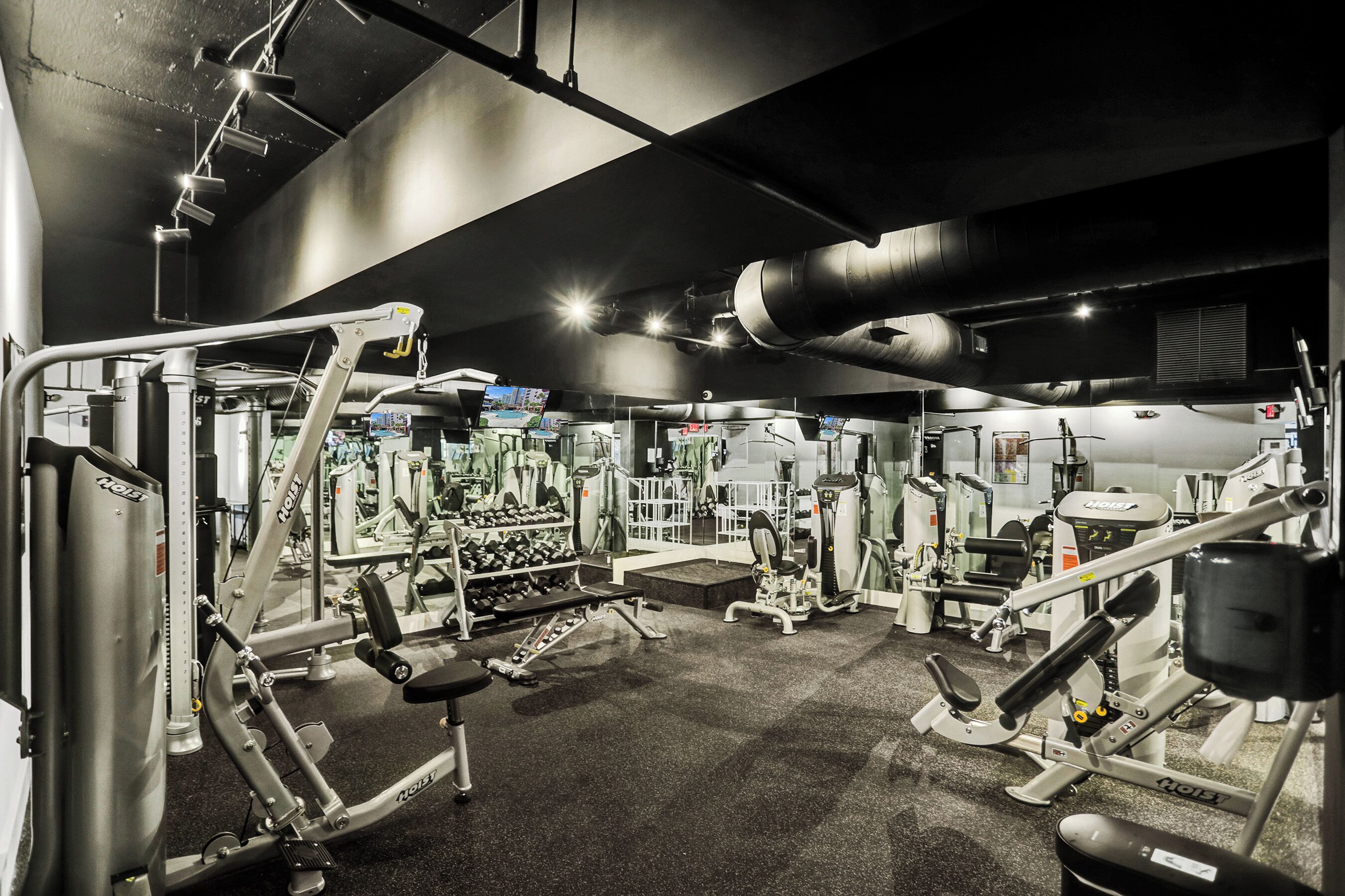 Ein Fitnessstudio mit verschiedenen Trainingsgeräten, Gewichten und einer Spiegelwand.