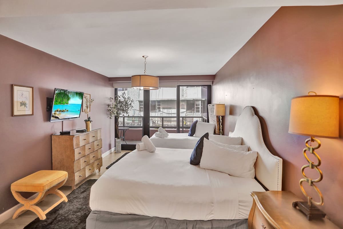 Quarto de hotel com uma cama grande, televisão, cômoda e vista para o exterior.