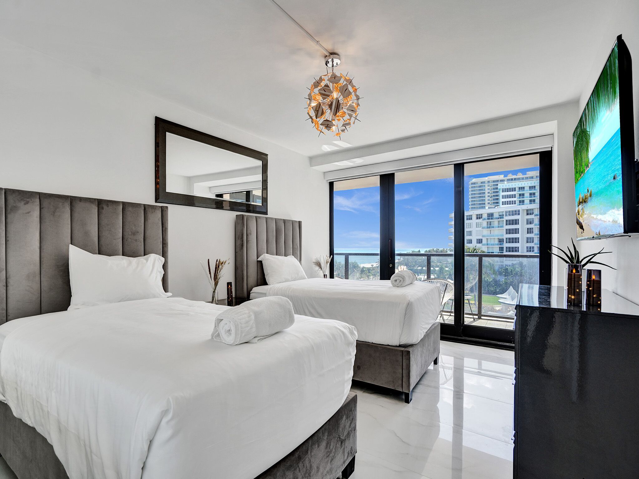Une chambre d’hôtel moderne avec deux lits, une grande fenêtre donnant sur la ville, un lustre et un téléviseur à écran plat.