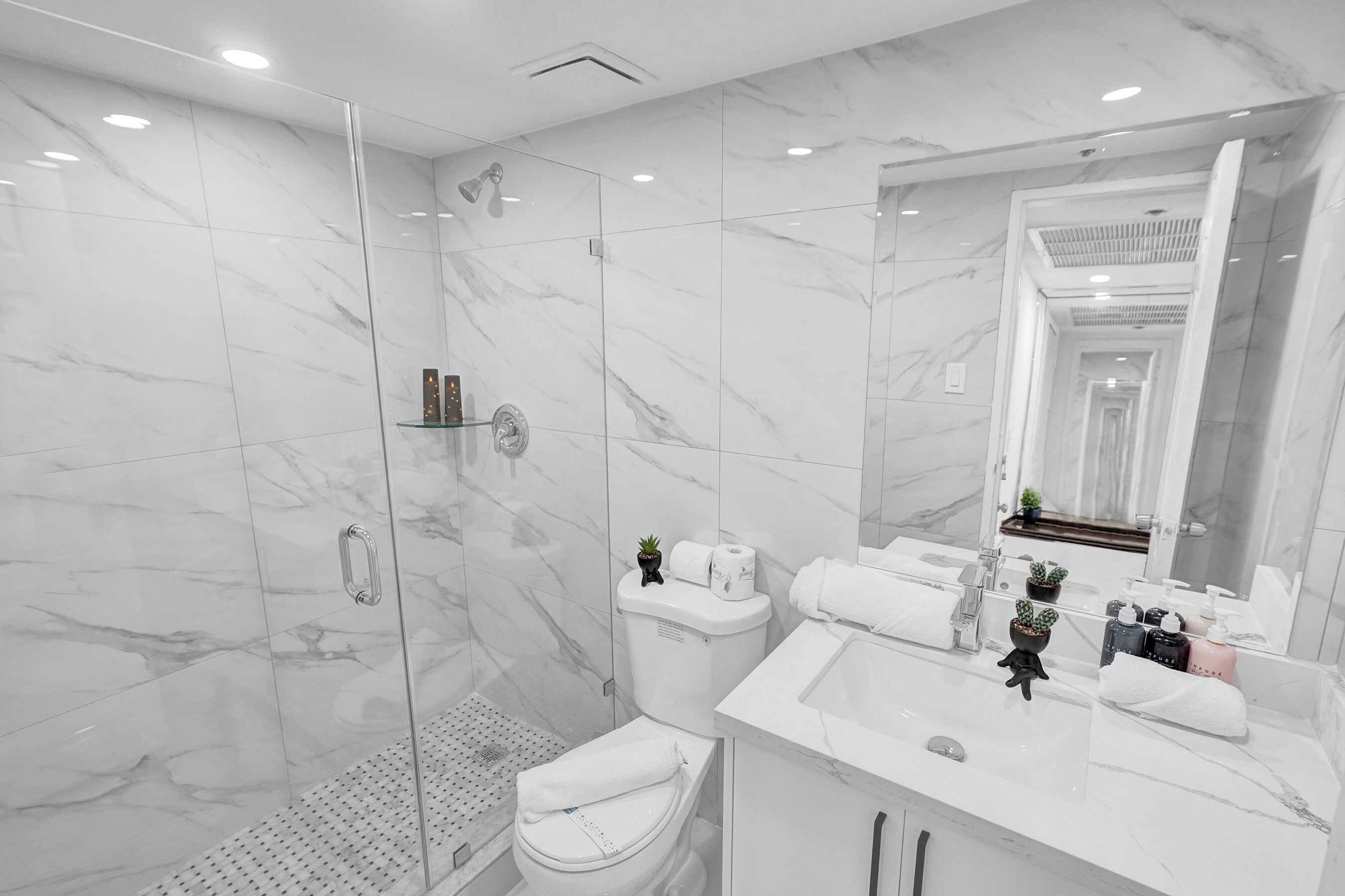 A modern bathroom with a glass shower enclosure, a toilet, and a sink with a mirror.