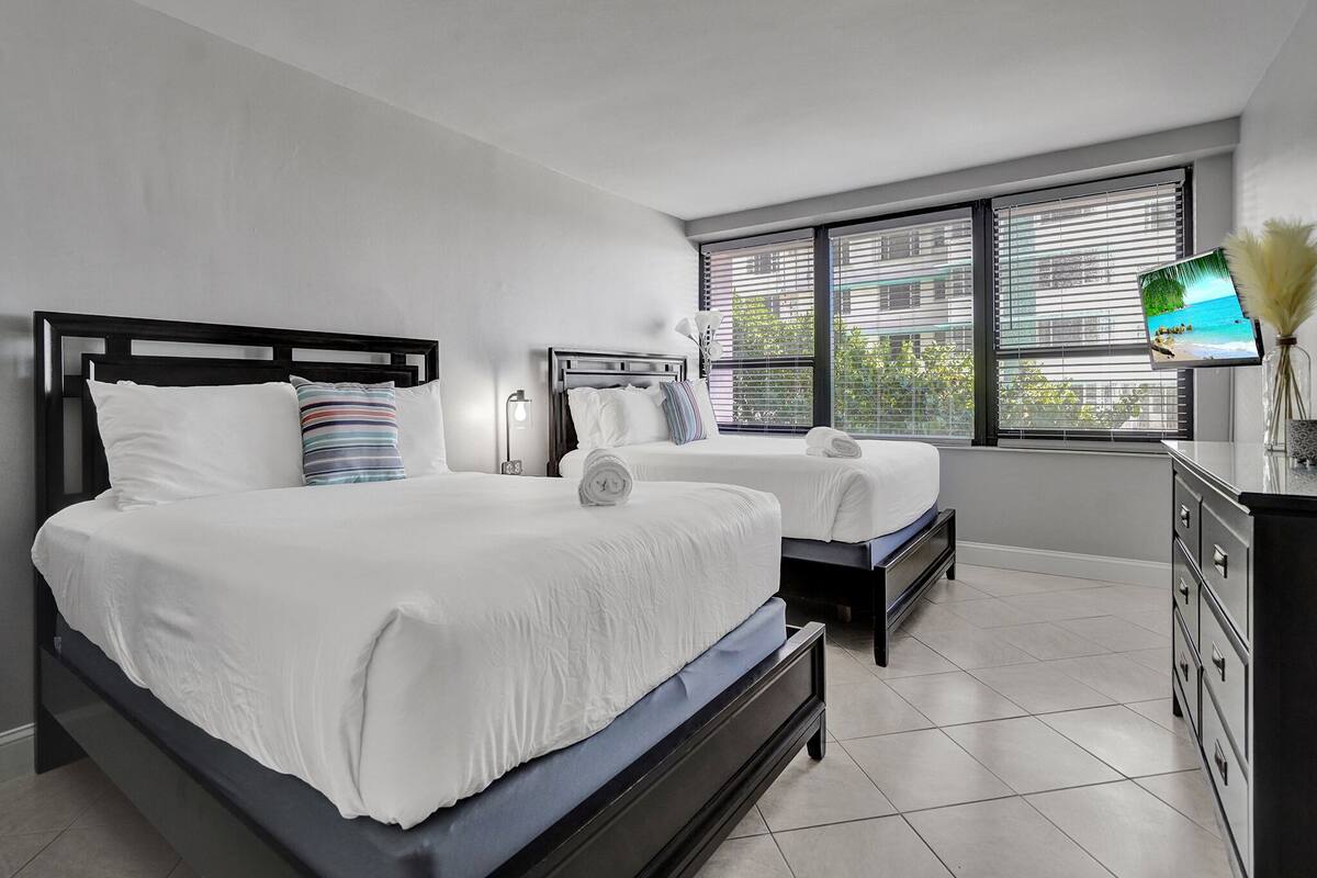 Quarto de hotel com duas camas, uma televisão e uma cômoda.