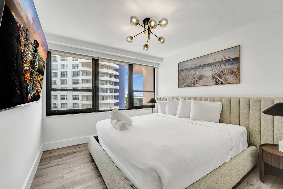 Quarto de hotel moderno com uma cama grande, vista para a cidade, um quadro e um lustre exclusivo.