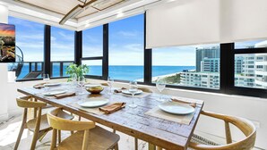 A dining area with a wooden table, chairs, and large windows offering a view of the ocean and buildings. - Alexander Hotel (Miami Beach)