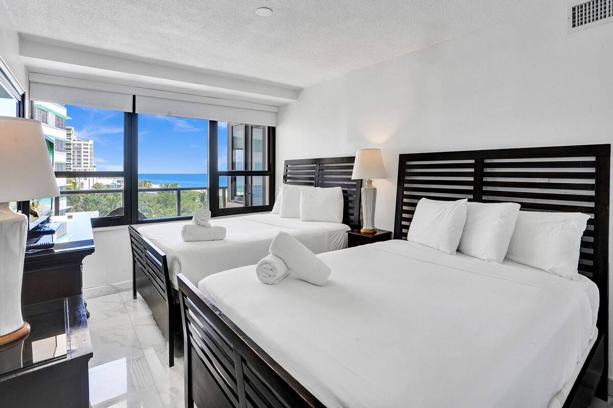 Quarto de hotel com duas camas, uma escrivaninha e vista para o oceano.