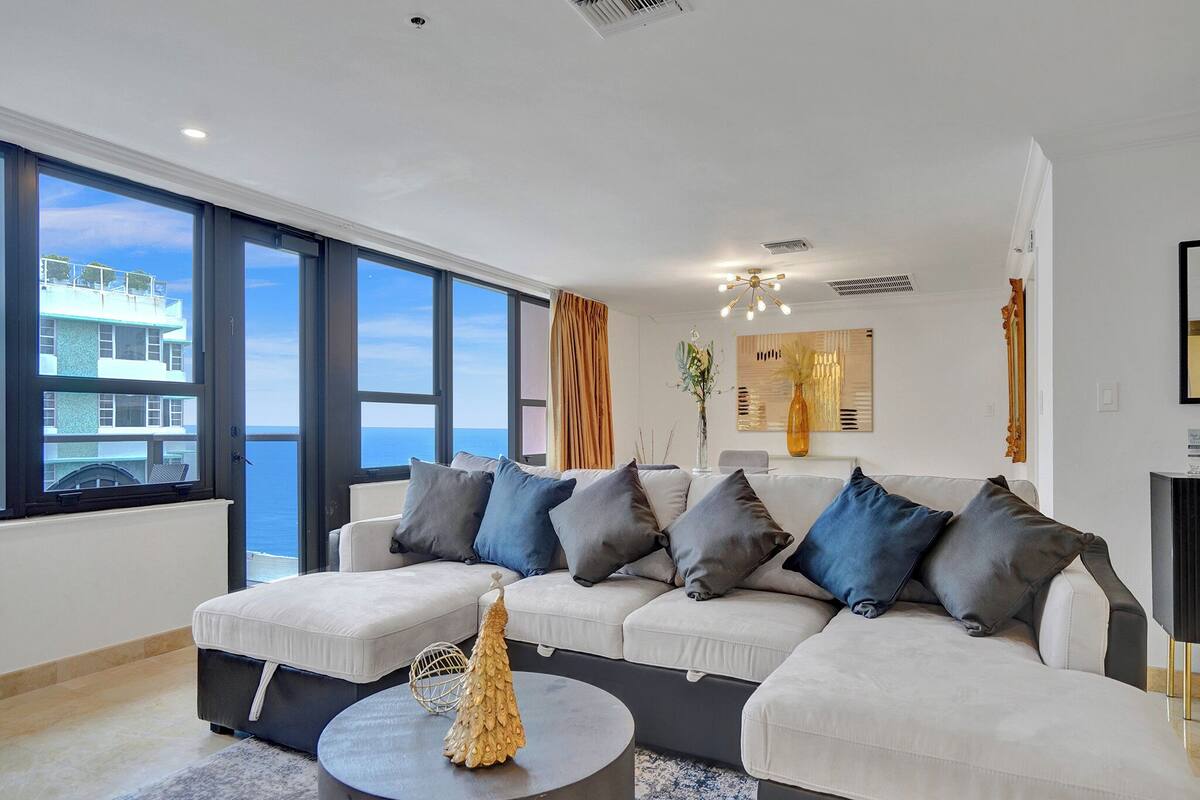 Sala de estar moderna com uma grande janela que oferece vista para o mar e um edifício.