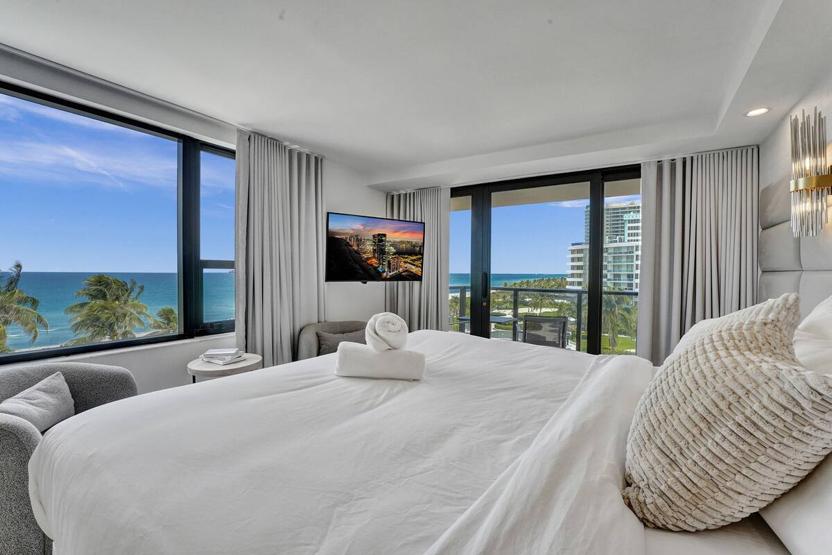 Quarto de hotel moderno com uma cama grande, televisão de tela plana e varanda com vista para a cidade.